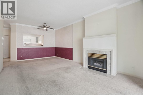Living room with beige carpet, fireplace with marble surround, and cut-out to kitchen. - 308 4728 53 Street, Delta