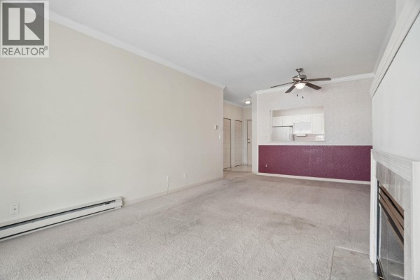 Living room with beige carpet, electric baseboard heater, and cut-out to kitchen. - 308 4728 53 Street, Delta