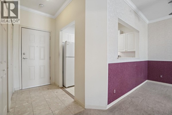 Apartment entryway with tiled floor, white door, and opening to kitchen with white appliances. - 308 4728 53 Street, Delta