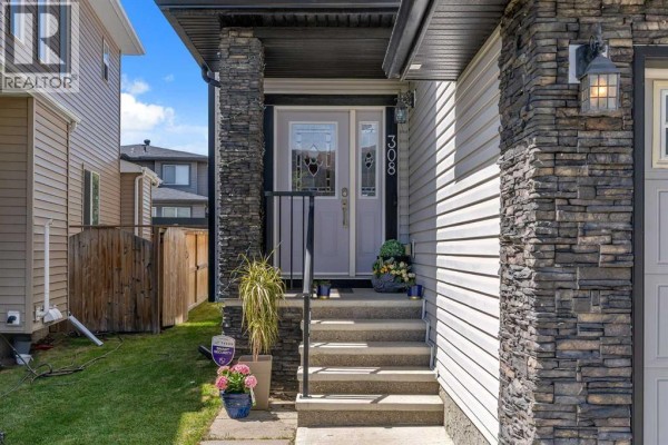 Front entrance of a residential home with a gray door, stone column accents, and a covered porch. - 308 Kinniburgh Link, Chestermere