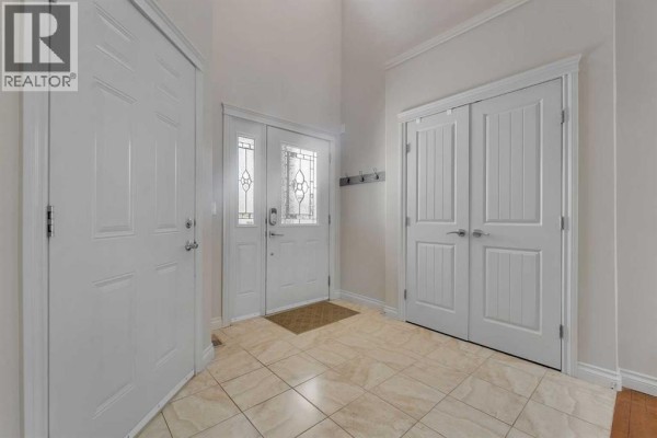 Interior view of a spacious entryway with a front door, tiled floor, and multiple closets with white doors. - 308 Kinniburgh Link, Chestermere