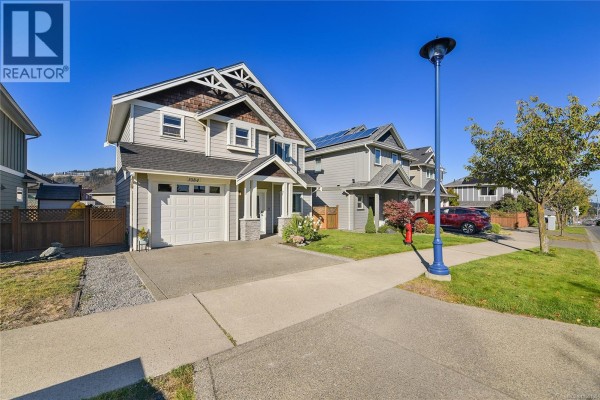 Street view of houses on a paved street with sidewalks, green lawns, and blue sky overhead. - 3084 Langford Lake Rd, Langford