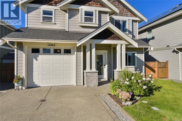 A closer front view of a two-story house, highlighting the garage door, entrance, and landscaping with stone pillars. - 3084 Langford Lake Rd, Langford