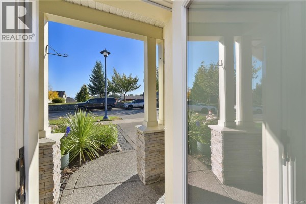 View from inside the covered entryway looking out at the walkway, landscaping, and street with parked cars. - 3084 Langford Lake Rd, Langford