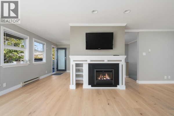 Living room with light wood floors, grey walls, a fireplace, and a television. - 3085 Maple Street, Vancouver