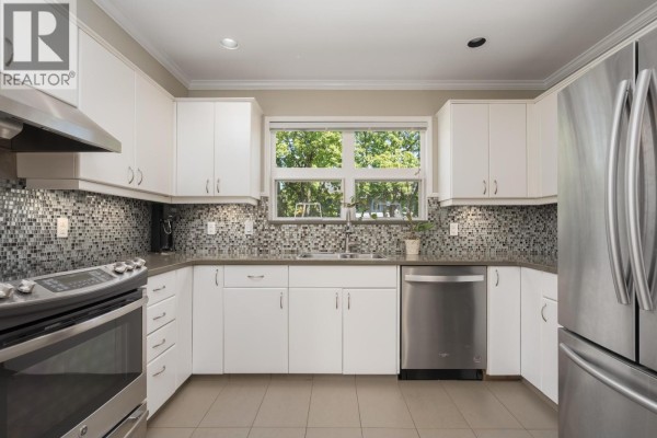 Kitchen with white cabinets, mosaic tile backsplash, stainless steel appliances, and a window. - 3085 Maple Street, Vancouver