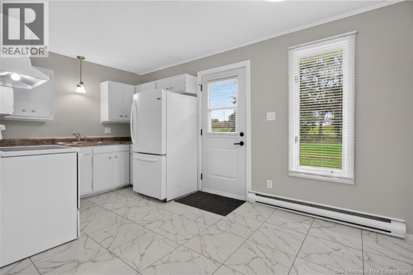 White kitchen with light grey walls, white cabinets, white appliances, and marble tile flooring. - 3086 Route 132, Scoudouc
