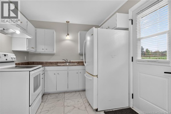 White kitchen with light grey walls, white cabinets, white appliances, and marble tile flooring. - 3086 Route 132, Scoudouc