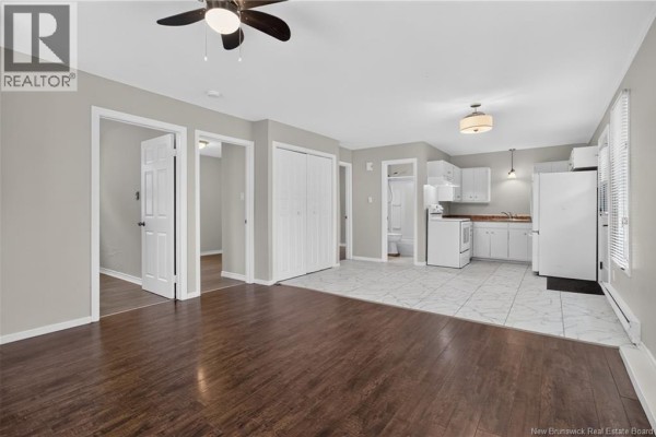 Open concept living area with dark wood floors connecting to a kitchen and two doorways. - 3086 Route 132, Scoudouc