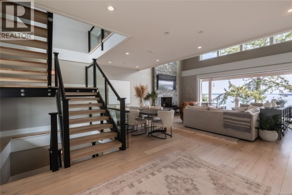 Living area with a dining table, fireplace, sectional sofa, and large windows overlooking the water. - 3089 Cook St, Chemainus