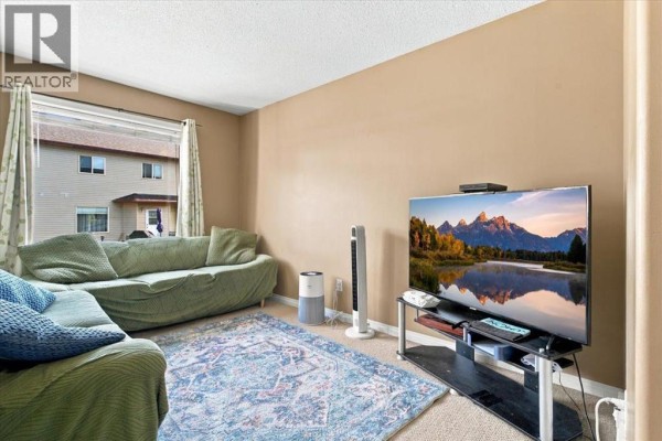 Living room with beige walls, a green couch, and a large TV. - 309, 10150 121 Avenue, Grande Prairie