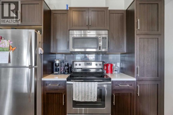 Compact kitchen with dark brown cabinets, stainless steel appliances, and a white quartz countertop. - 309, 250 Fireside View, Cochrane