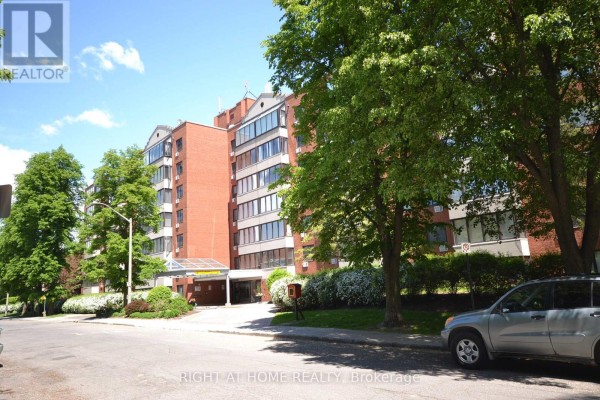 Side view of a red brick apartment building with mature trees and landscaping. - 309 - 225 Alvin Road N, Ottawa
