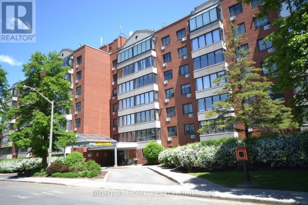 Front exterior of a multi-story brick apartment building with a glass entrance canopy. - 309 - 225 Alvin Road N, Ottawa