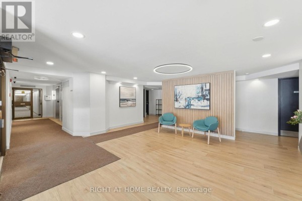 Modern building lobby with wood floors, teal chairs, and abstract wall art. - 309 - 225 Alvin Road N, Ottawa