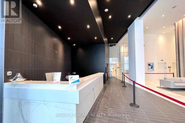 Modern condo lobby with a marble reception desk, dark tile walls, and bright lighting. - 309 - 3900 Confederation Parkway, Mississauga