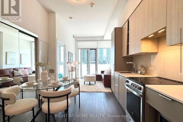 Apartment kitchen with stainless steel appliances, wood cabinets, and a view of the living area. - 309 - 3900 Confederation Parkway, Mississauga