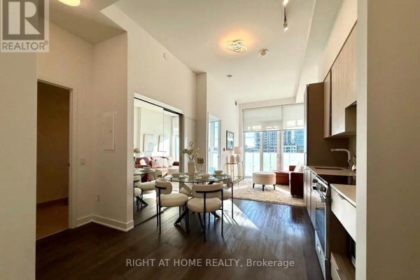 Open concept apartment dining area with a glass table and living room with brown sofa. - 309 - 3900 Confederation Parkway, Mississauga