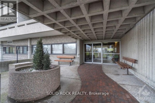Entrance to the apartment building with brick walkway, concrete benches, and planters. - 309 - 415 Greenview Avenue, Ottawa
