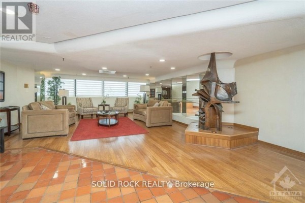 Lobby seating area with beige sofas, armchairs, coffee tables, red rug, and sculpture. - 309 - 415 Greenview Avenue, Ottawa
