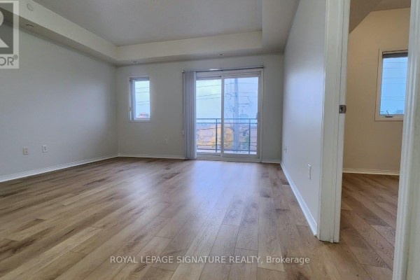 Living room with light wood floors, white walls, and a sliding glass door to a balcony. - 309 - 5150 Winston Churchill Boulevard, Mississauga