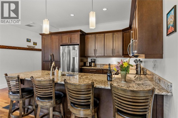 Bar seating at kitchen island with dark wood finishes and modern appliances. - 309 1 Street W Unit# 301, Revelstoke