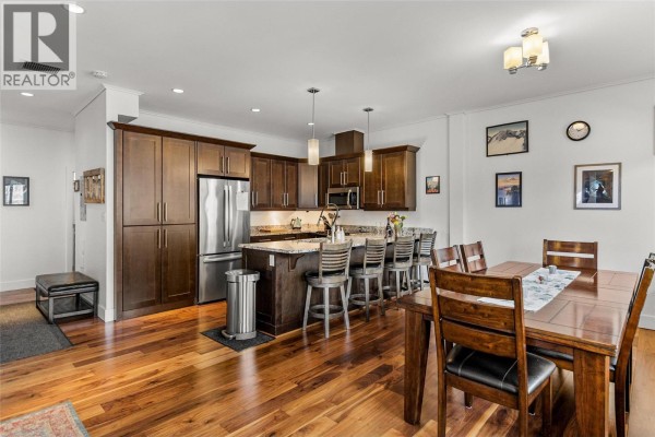 Dining area adjacent to kitchen with wooden table, chairs, and decorative wall art. - 309 1 Street W Unit# 301, Revelstoke