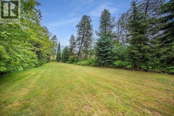 Large grassy lawn surrounded by tall green trees and foliage. - 309 12th Avenue, Genelle