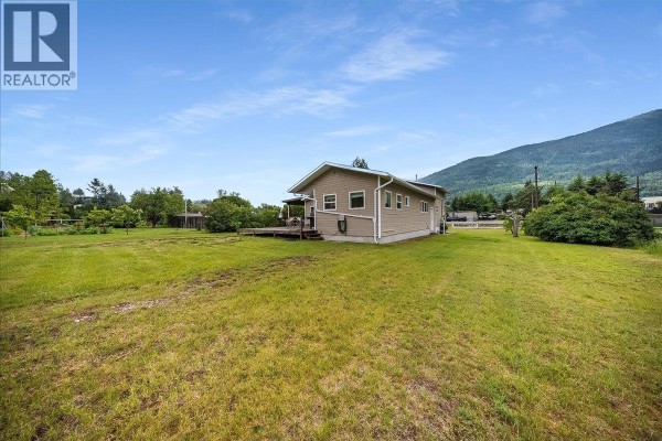 View of a tan-sided house with a wooden deck and a large grassy yard. - 309 12th Avenue, Genelle