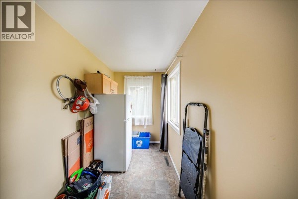 Narrow room with a refrigerator, storage cabinets, and a window with sheer curtains. - 309 12th Avenue, Genelle