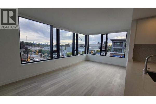 Living room with floor-to-ceiling windows offering views of the street and surrounding buildings. - 309 1616  Lloyd Avenue, North Vancouver