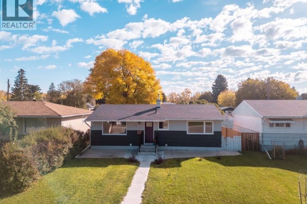 Aerial view of a bungalow with grey siding, a burgundy door, and a large tree with yellow leaves in the front yard. - 309 26 Street S, Lethbridge