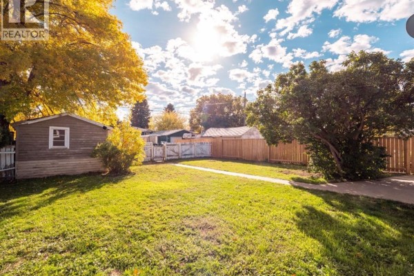 Backyard view with a lawn, trees, a wooden fence, a shed, and a detached garage. - 309 26 Street S, Lethbridge