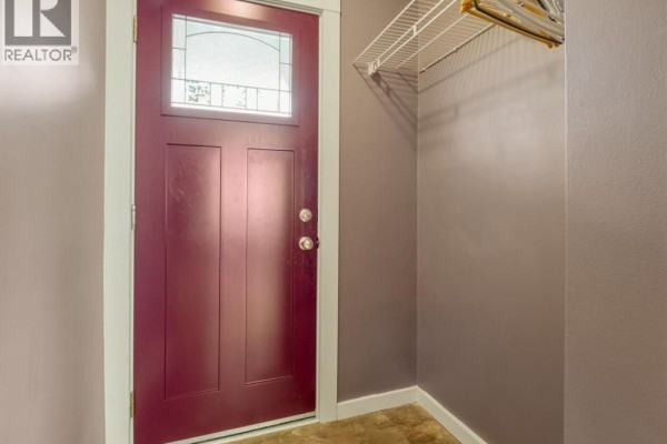 Close-up of a burgundy front door with a stained-glass window, next to a purple wall and a white wire shelf. - 309 26 Street S, Lethbridge