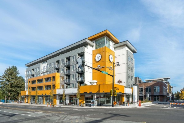 Corner view of a contemporary apartment building with orange accents and a clock tower. - 309 27215 Aldergrove Town Centre Drive, Langley