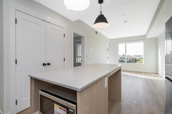 Kitchen with white and wood cabinets, an island with a microwave, and stainless steel appliances. - 309 27215 Aldergrove Town Centre Drive, Langley