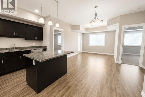 Modern kitchen with dark wood cabinets, granite countertops, stainless steel appliances, and island. - 309 412 Willowgrove Square, Saskatoon
