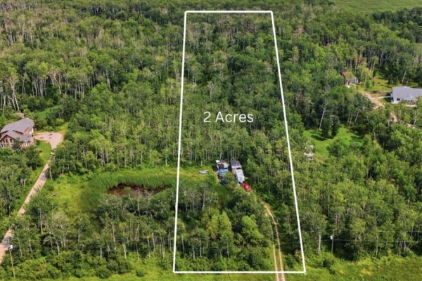 Aerial view of a 2-acre lot surrounded by trees, featuring a small pond and outbuildings. - 309 East Lakeshore Road, St Malo