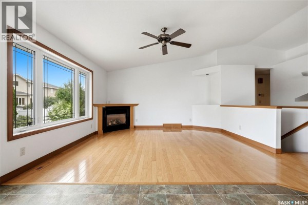 Living room with hardwood floors, gas fireplace, ceiling fan, and large bay window. - 3090 Cranbourn Crescent, Regina
