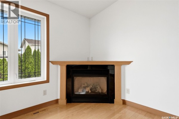 Close-up of a gas fireplace with a light wood mantel and black surround. - 3090 Cranbourn Crescent, Regina
