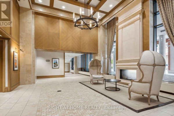 Spacious building lobby with beige stone walls, a decorative fireplace, and upholstered chairs. - 905 - 3091 Dufferin Street, Toronto