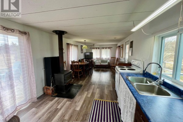 Wide view of the open-concept kitchen and living area in the mobile home, including a wood stove and seating. - 3092 Scotch Bush Road, Bonnechere Valley
