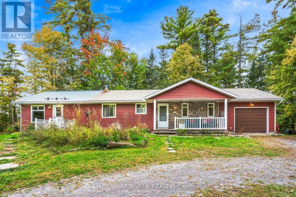 Red siding bungalow with stone accents, white porch railing, and attached garage. - 3099 8th Concession North Road, Mississippi Mills