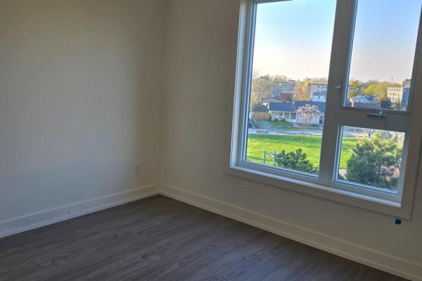 Empty room with white walls, dark wood laminate flooring, and a large window overlooking a park. - 309b - 16 Melbourne Avenue, St  Catharines