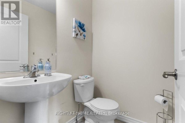 Powder room with a white pedestal sink, toilet, and a wall-mounted floral art piece. - 31 - 7945 Oldfield Road, Niagara Falls