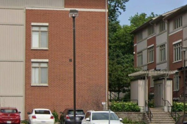 Side view of brick townhouses with windows, parking lot, and mature trees in the background. - 1 - 795 Montreal Road, Ottawa