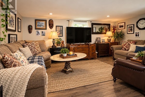 Living room with a sectional sofa, leather armchair, large television, and decorative items on walls. - 31-15 Fish Hatchery Rd, Sault Ste  Marie