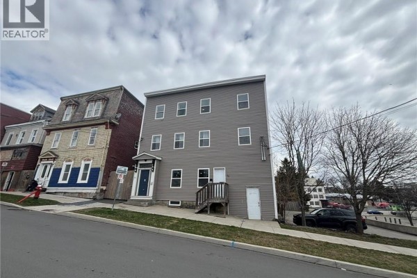 Angle view of a grey multi-family building showing multiple windows and adjacent historic buildings. - 31-33 Peters Street, Saint John