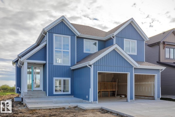 Side view of a blue two-story house under construction with Tyvek wrap and unfinished garage doors. - #31 3410 Ste Anne Trail, Rural Lac Ste  Anne County
