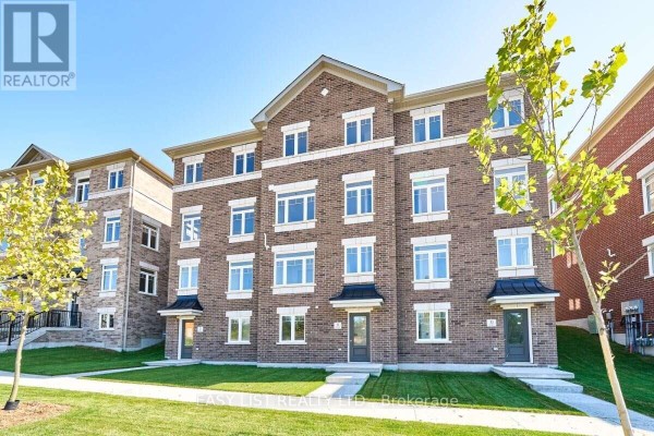 View of the front facade of a brick townhouse development under a clear blue sky. - 31 Addyman Crescent, Clarington